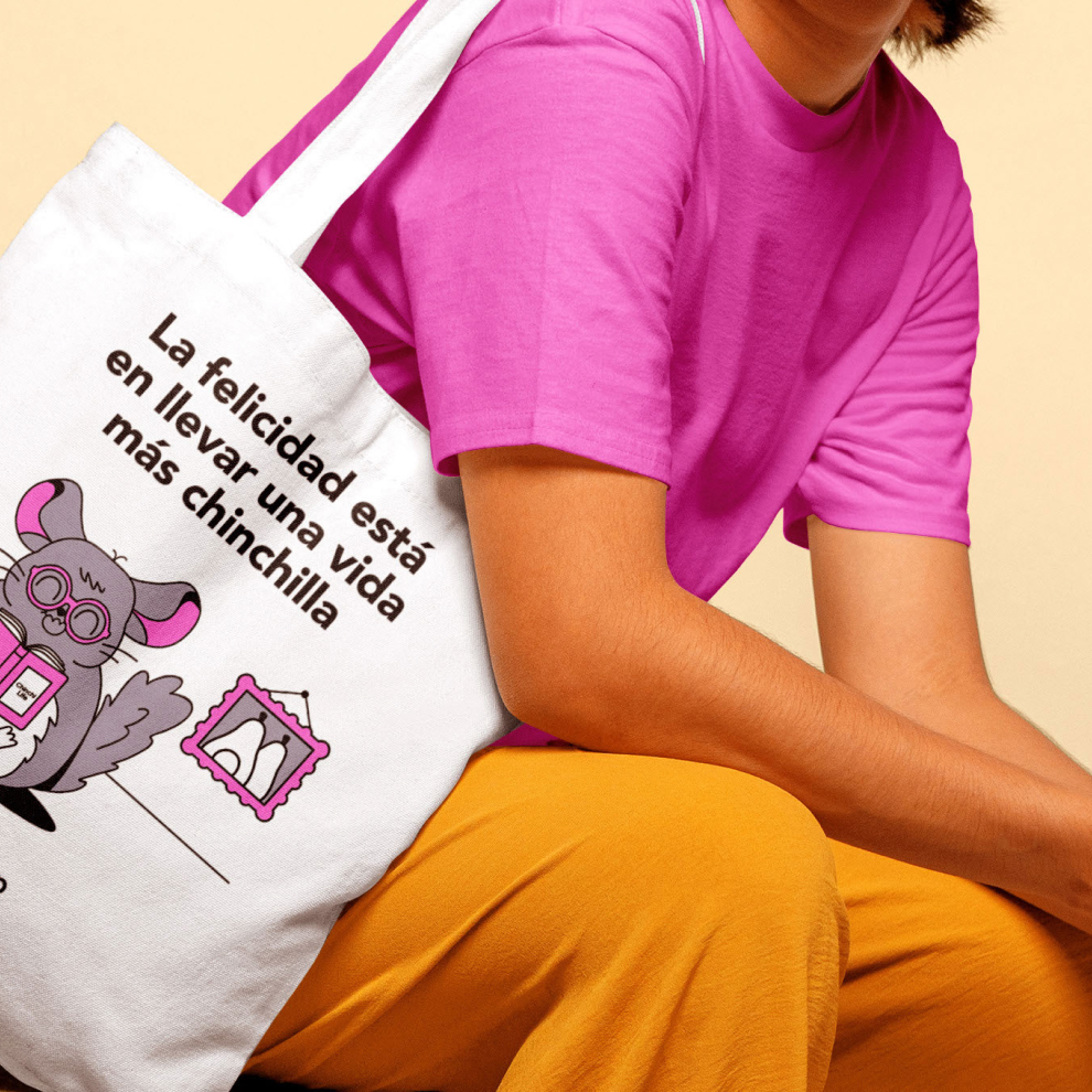 Una fotografía de revista muestra a una mujer posando con una bolsa tote que tiene la frase “La felicidad está en llevar una vida más chinchilla”. También se puede ver la ilustración de una chinchilla disfrutando una tarde de lectura en su hogar.